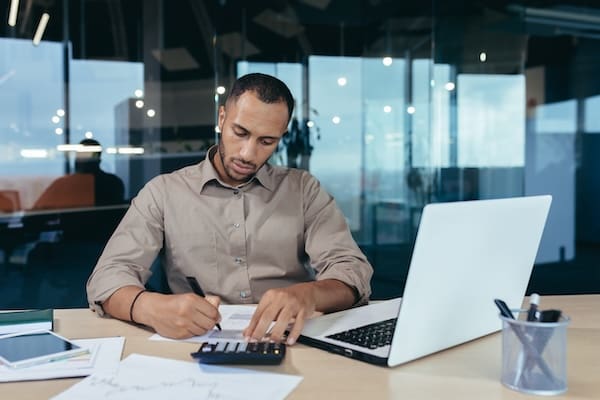 Trends in government contracting, represented by a man writing at a desk, with a laptop and calculator in front of him.